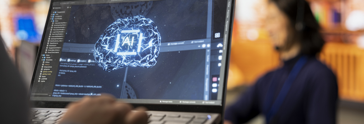 A imagem mostra um computador com um cérebro digital “AI” no ecrã, representando a Inteligência Artificial e a tecnologia digital.