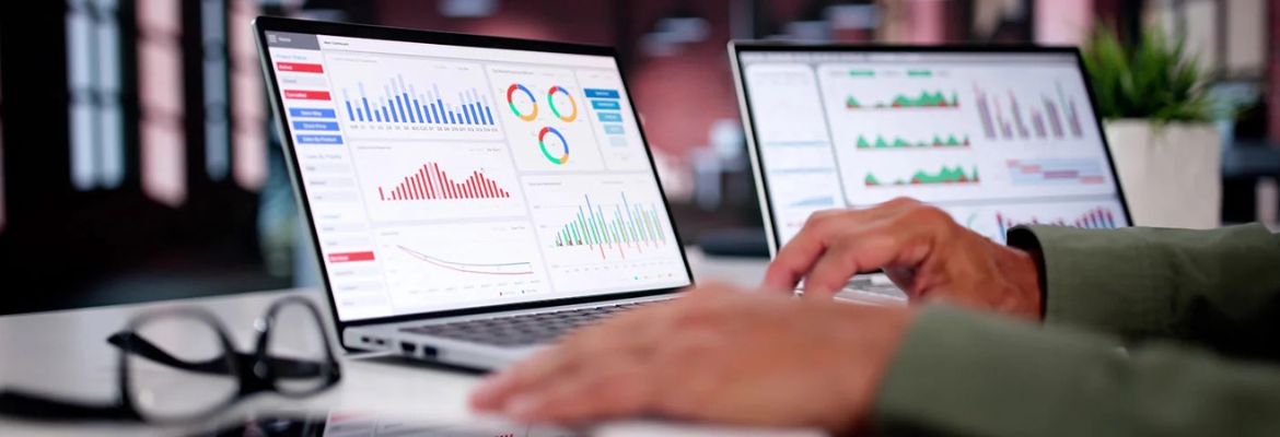 Profissional a analisar dados de marketing digital com gráficos e métricas num portátil e tablet, representando digital marketing analytics